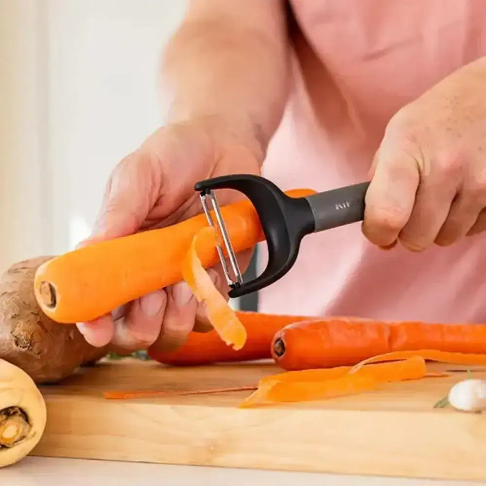 Person using a carrot peeler to peel carrots on a wooden cutting board.