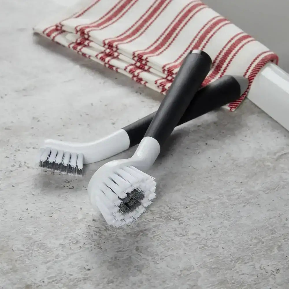 Two cleaning brushes with scrubber heads on a concrete surface with a red and white striped towel in the background.