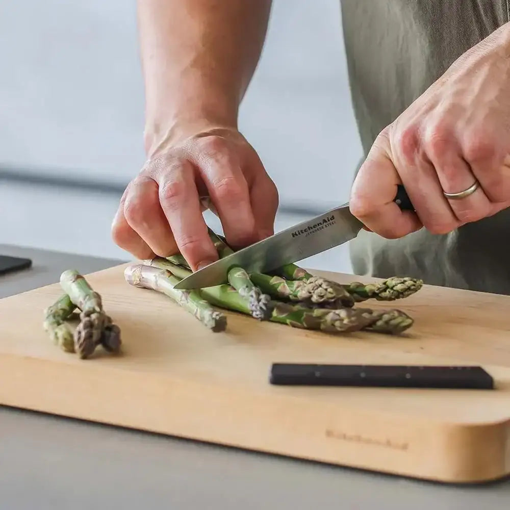 Person cutting asparagus on a wooden cutting board with a knife