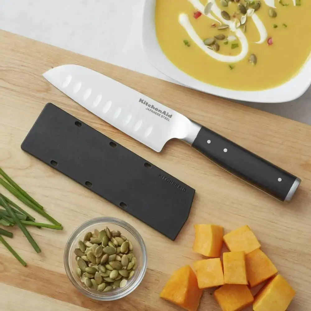 KitchenAid knife on a wooden cutting board with vegetables and soup in the background