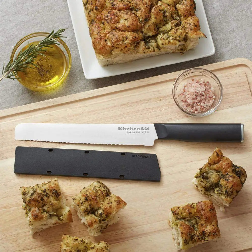 Wooden cutting board with sliced bread, a knife, and small bowls of oil and salt.