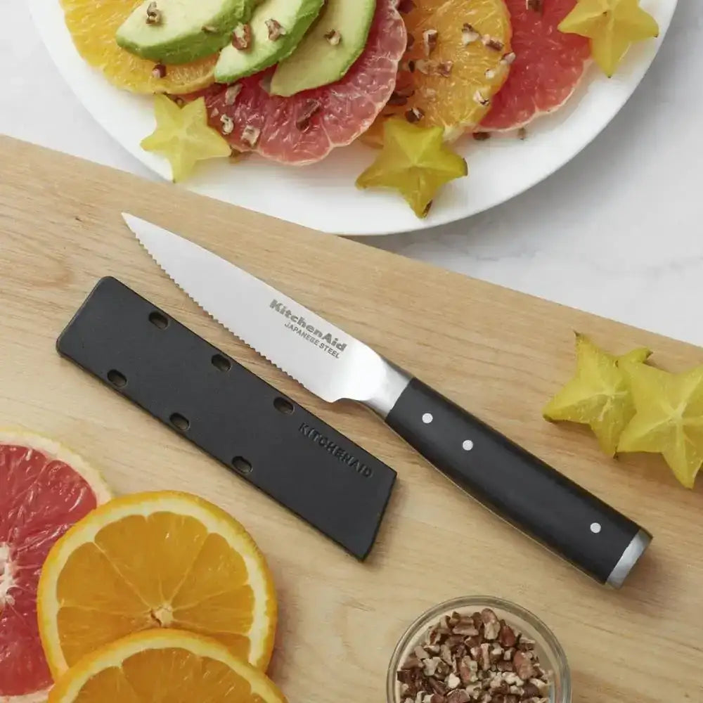 Knife with black handle and blade on a wooden cutting board with sliced fruits in the background