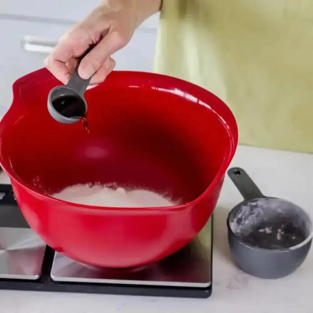 Person pouring liquid into a red mixing bowl on a stove