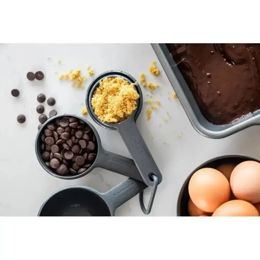 Baking ingredients including chocolate chips, brown sugar, eggs, and a pan of brownie batter on a white surface.