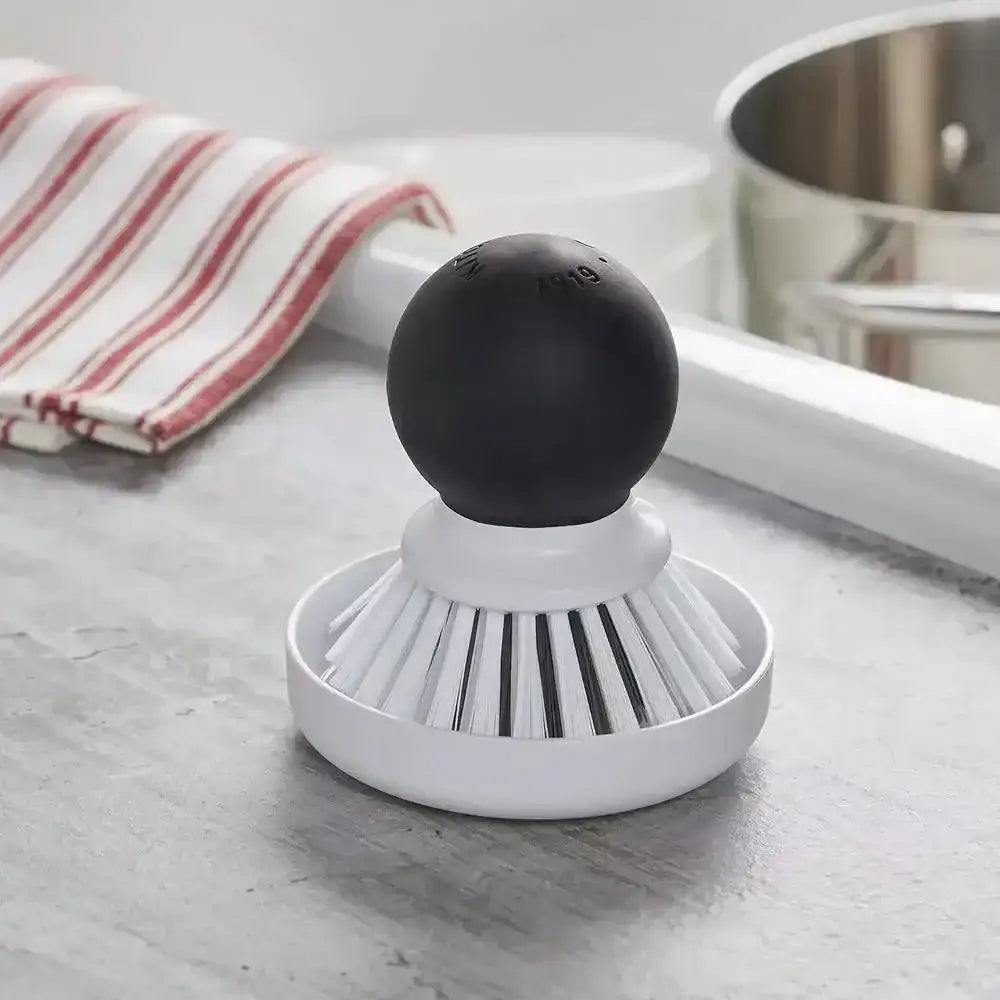 Black and white kitchen scrubber on a light gray surface with a striped towel and pot in the background.