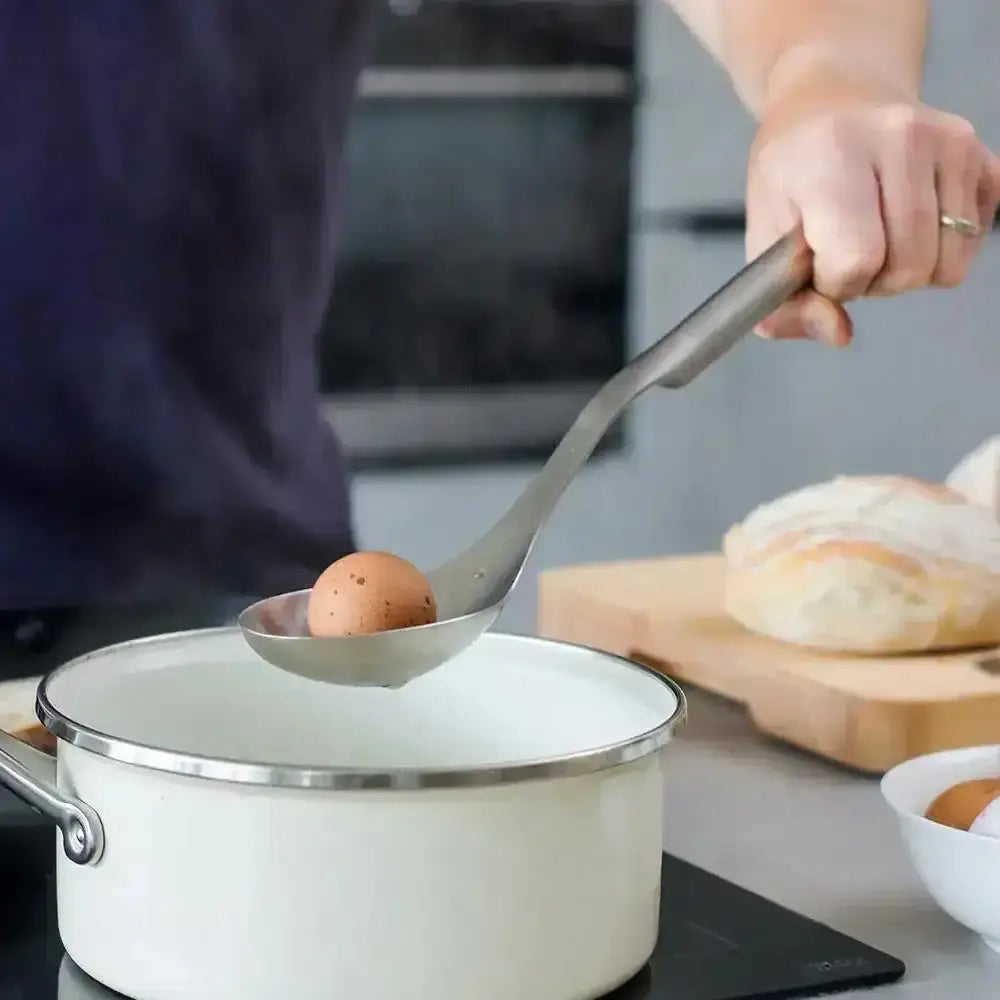 Person using a ladle to scoop an egg from a pot on a kitchen counter.