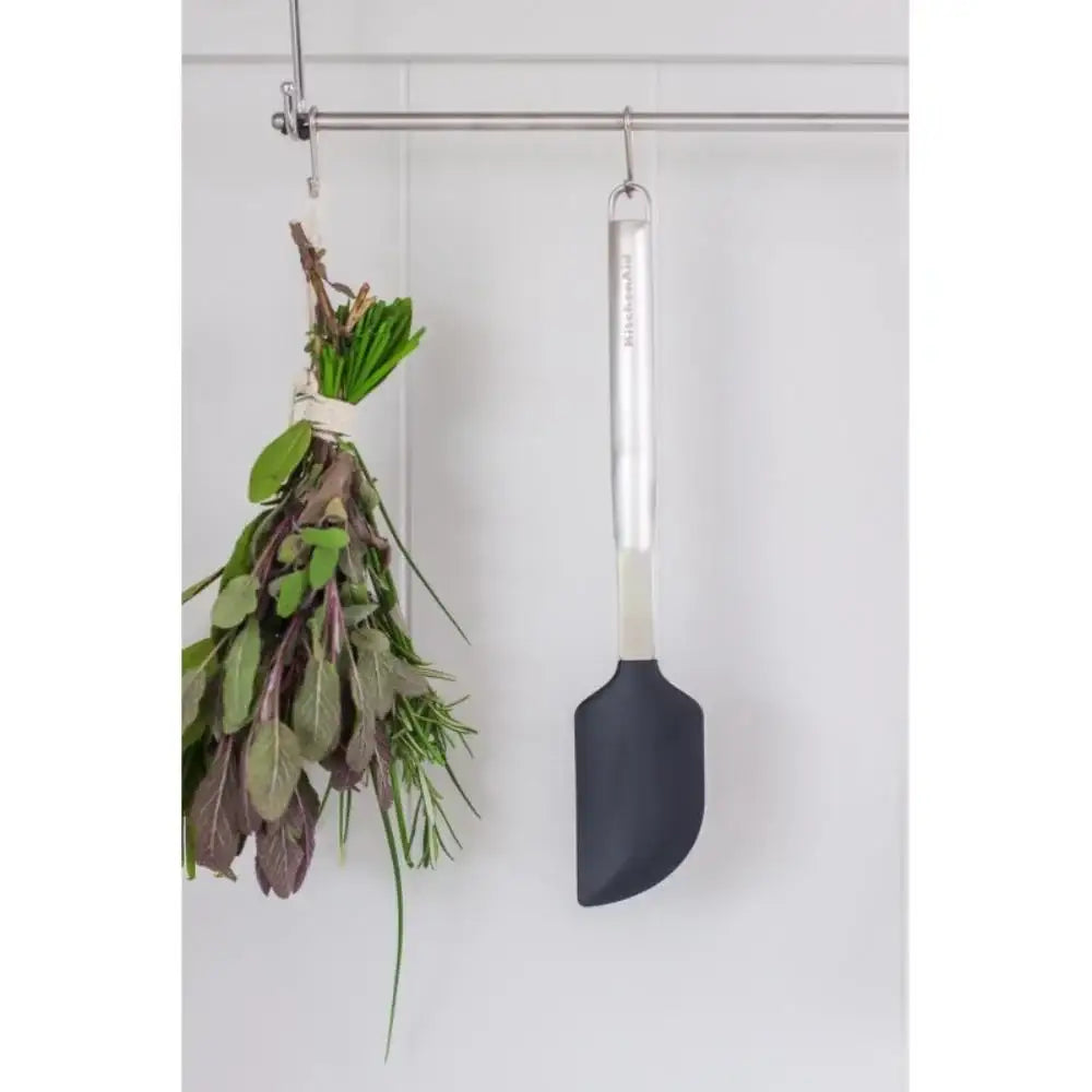 Herbs hanging on a hook next to a black spatula with a white handle on a light gray background