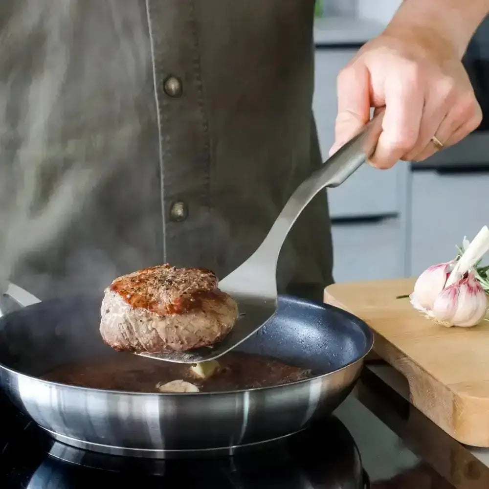 Person cooking a patty in a frying pan with a wooden cutting board in the background