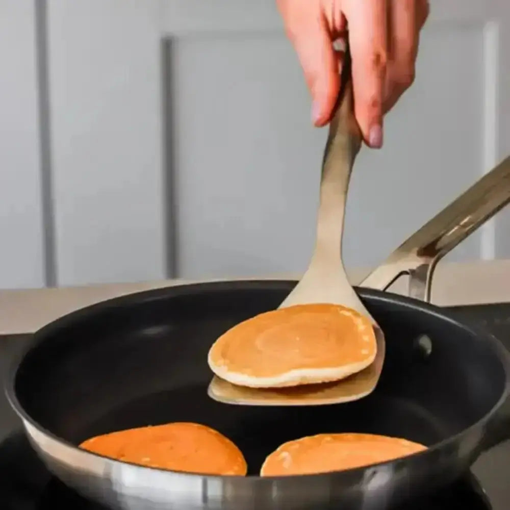 Person flipping pancakes in a pan with a spatula.