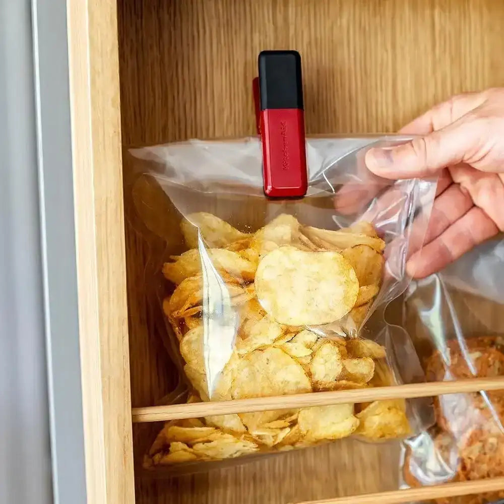 Person using a red and black clip to seal a bag of chips inside a wooden cabinet.