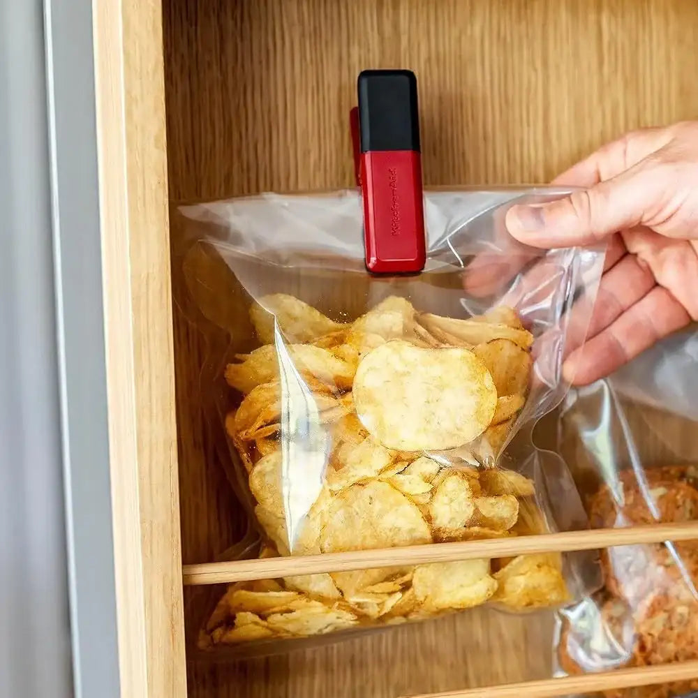 Person using a red and black clip to seal a bag of chips inside a wooden cabinet.