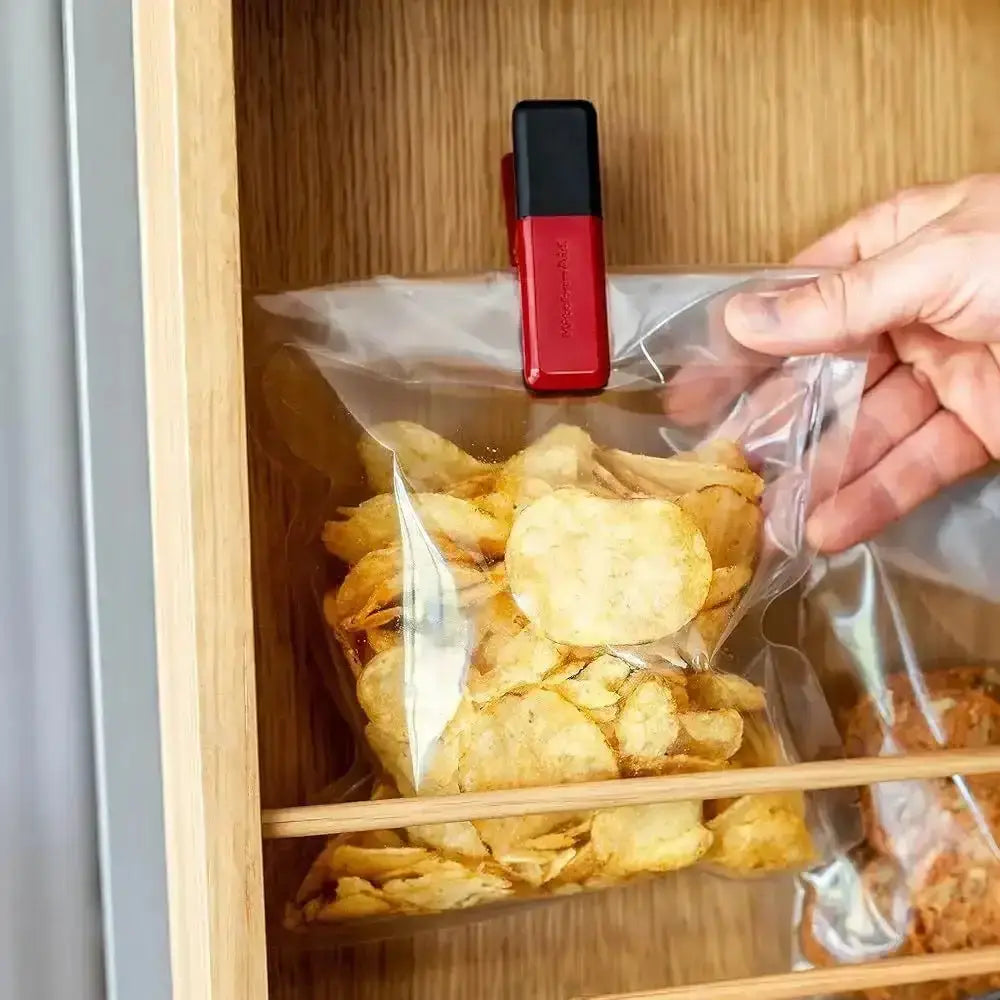Person using a red and black clip to seal a bag of chips inside a wooden cabinet.