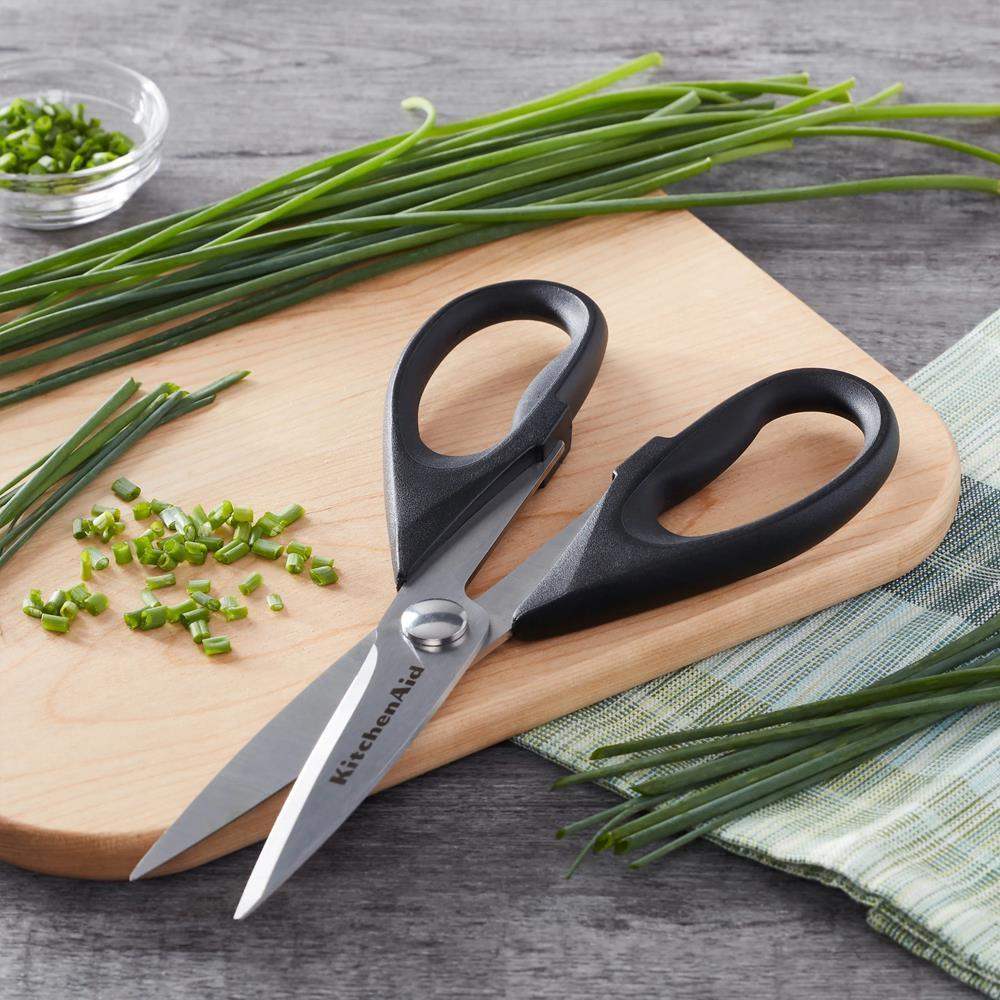 Kitchen shears on a wooden cutting board with chopped green onions