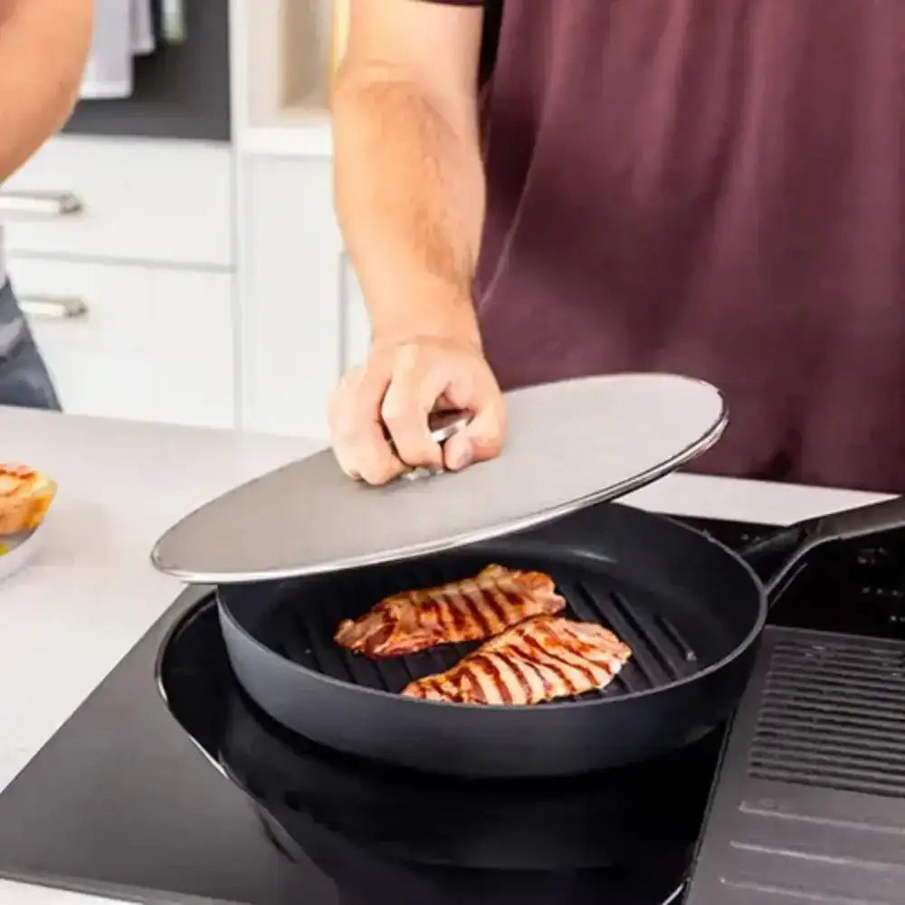 Person cooking steak in a pan with a lid on a stove