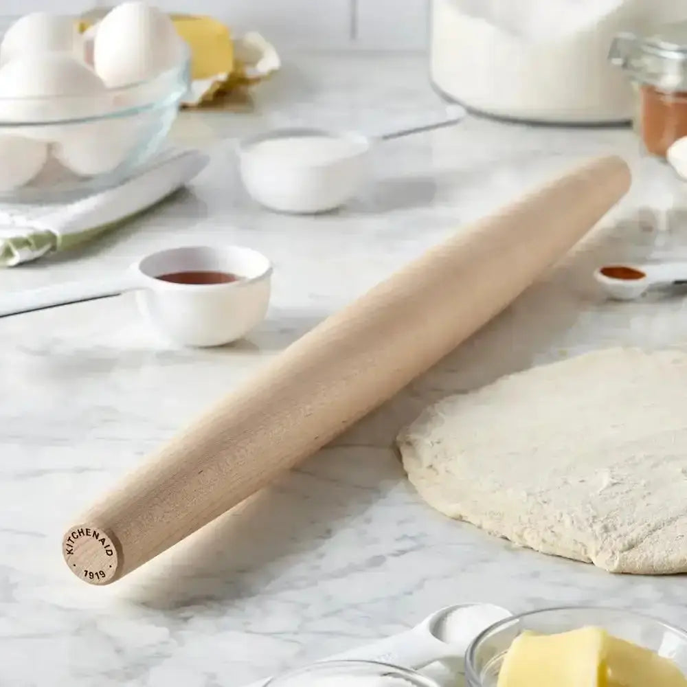 Wooden rolling pin on a marble surface with baking ingredients.