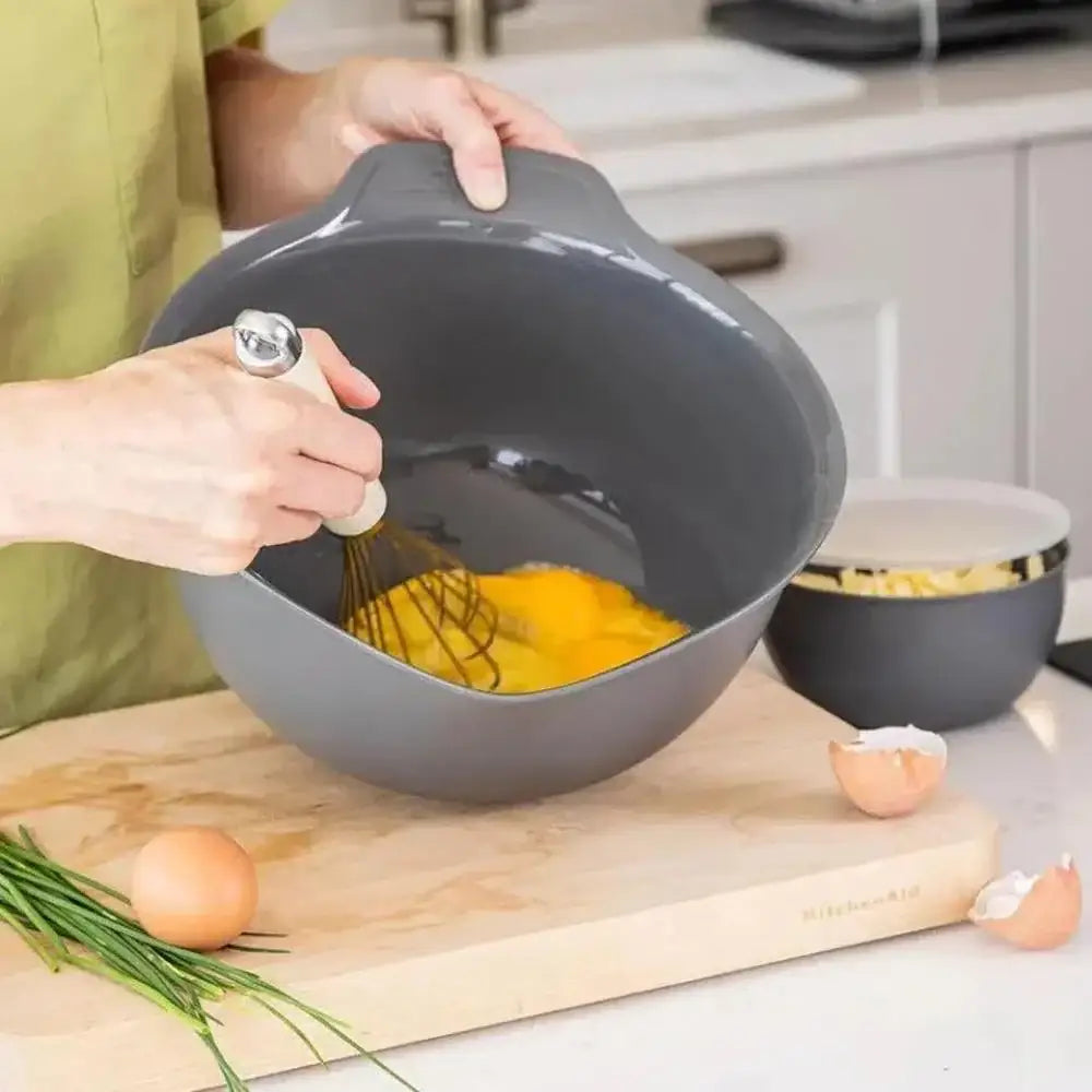 Person whisking eggs in a gray bowl on a kitchen counter.