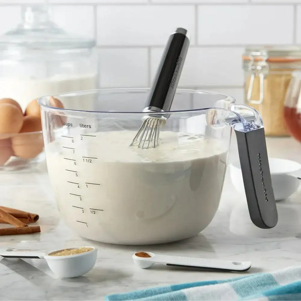 Clear measuring cup with whisk and ingredients on a kitchen counter