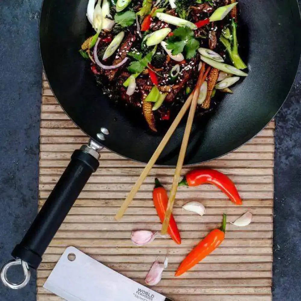 Frying pan with stir-fry dish on a wooden board, surrounded by ingredients.