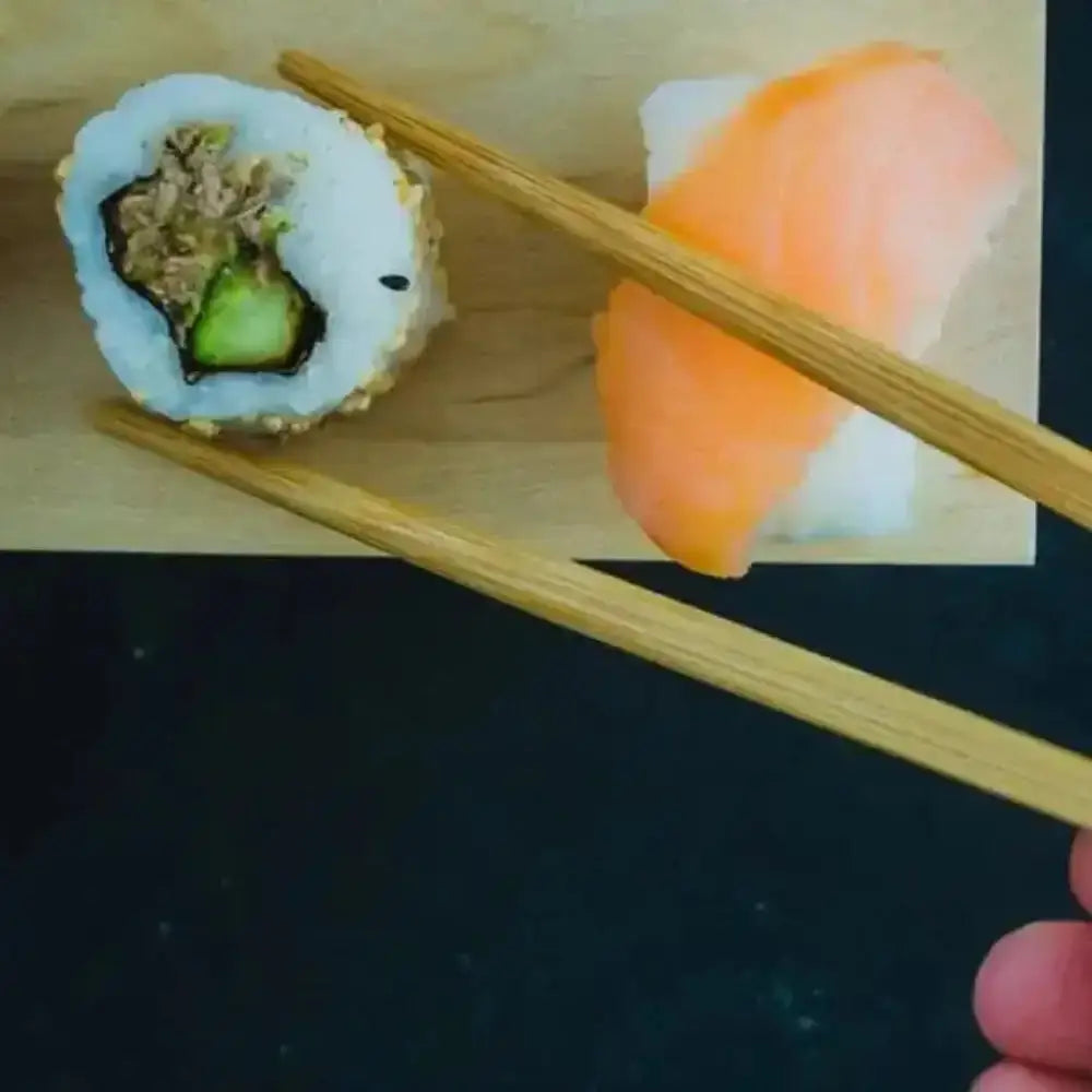 Sushi roll with avocado and salmon on a wooden board with chopsticks.
