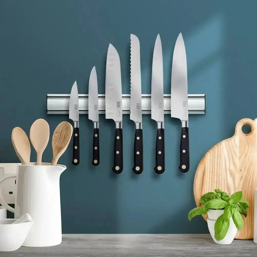 Set of knives with black handles on a magnetic strip against a blue wall, with kitchen utensils and decor items below.