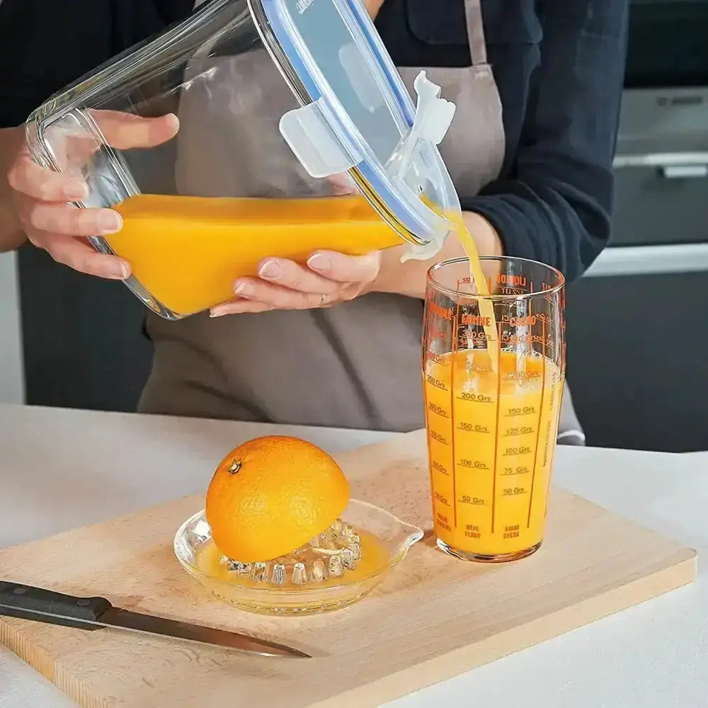 Person pouring orange juice from a container into a glass on a kitchen counter.