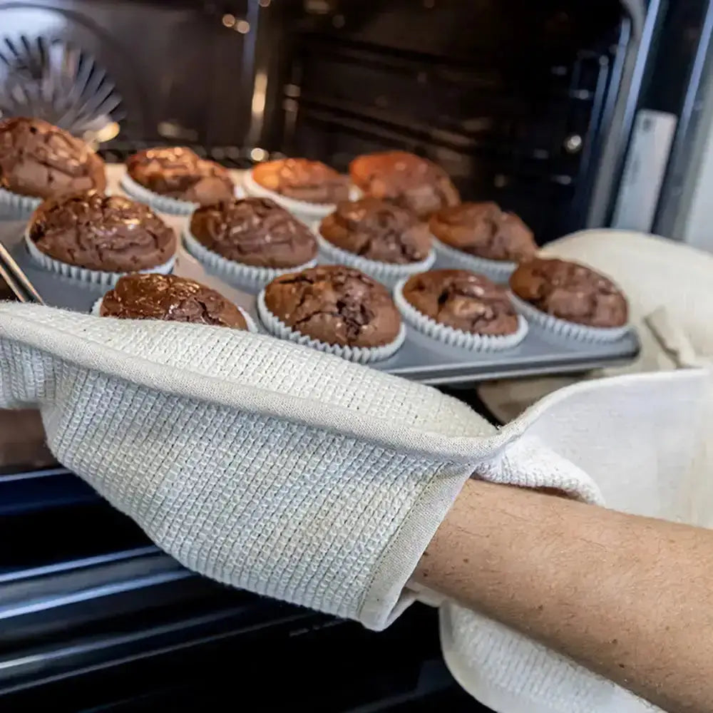Person wearing an oven mitt removing a tray of chocolate cupcakes from an oven.