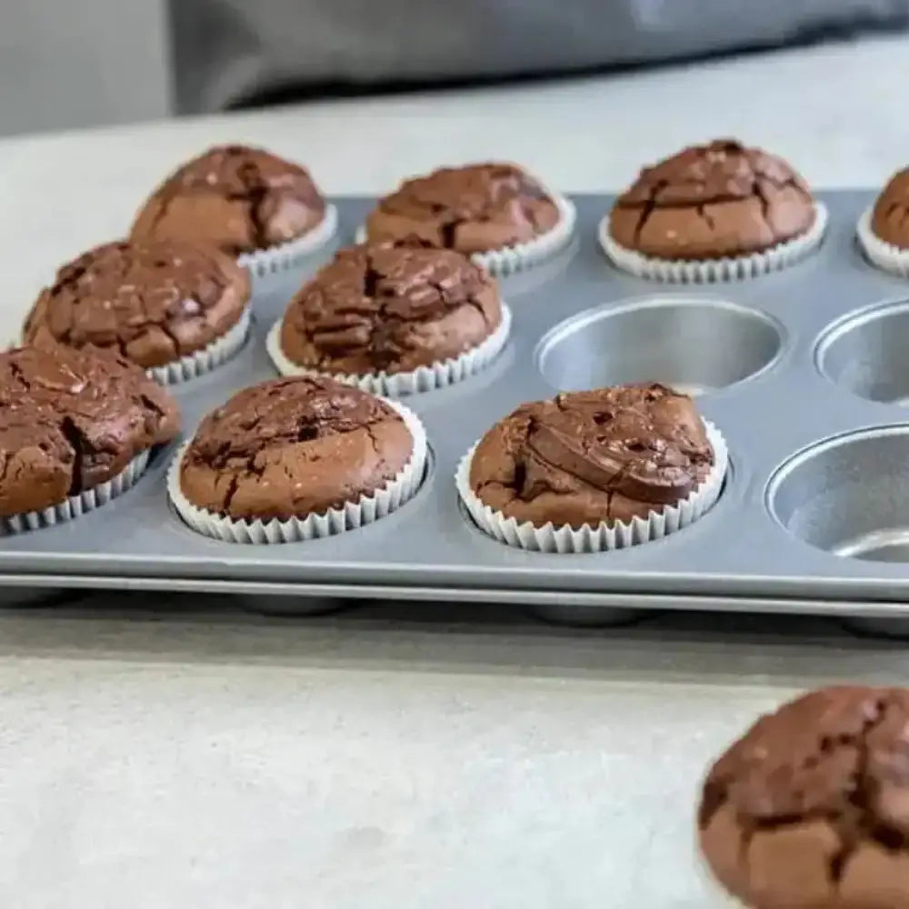 Baked chocolate cupcakes in a muffin tin on a kitchen counter.