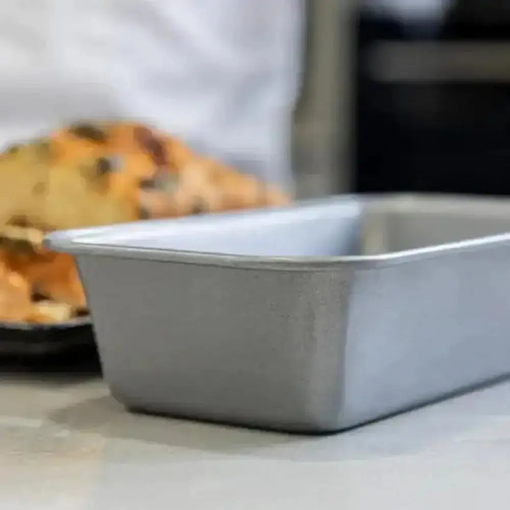 Metal loaf pan on a kitchen counter with a blurred background of food.