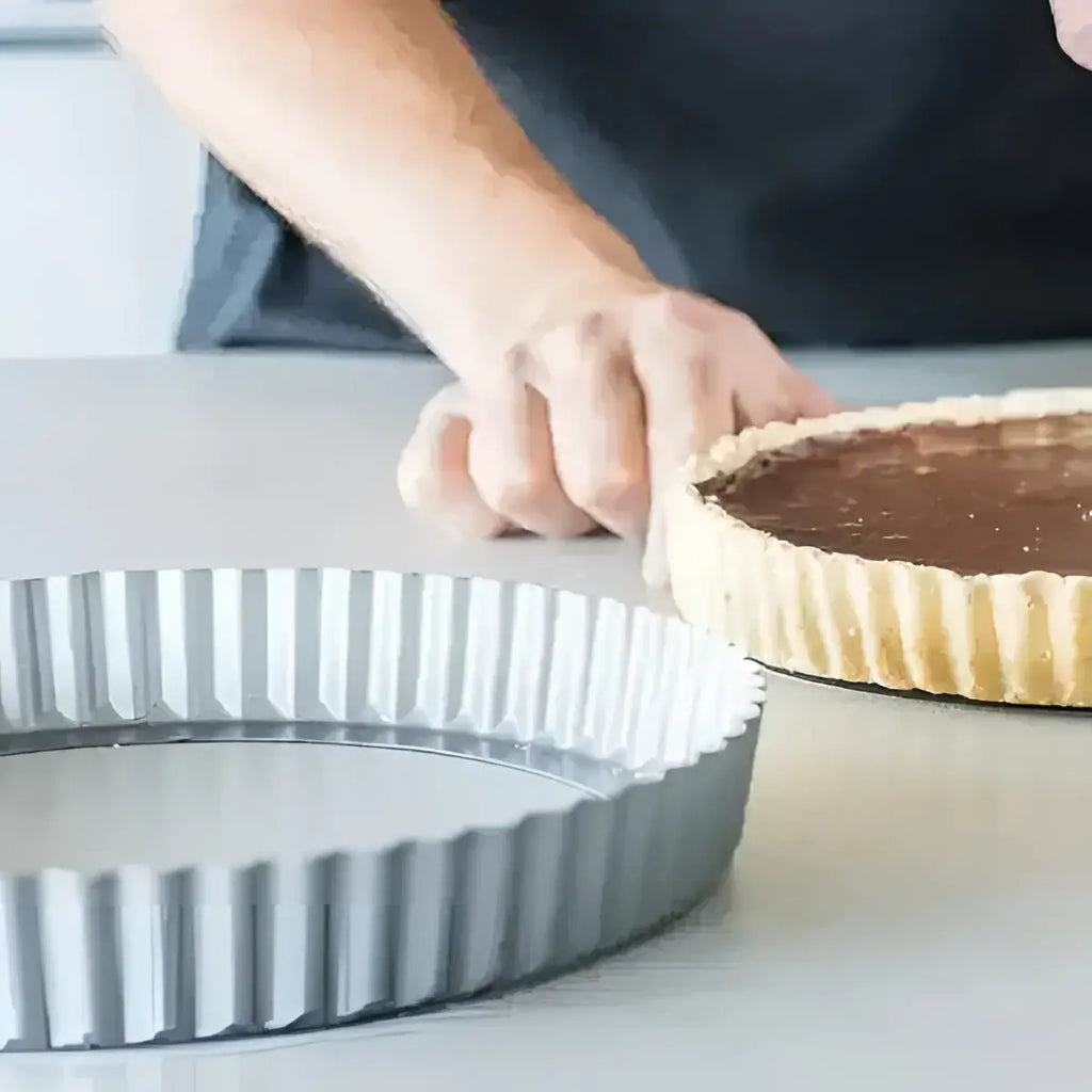 A fluted metallic silver KitchenCraft non-stick loose base flan tin 24.5cm beside a baked chocolate tart