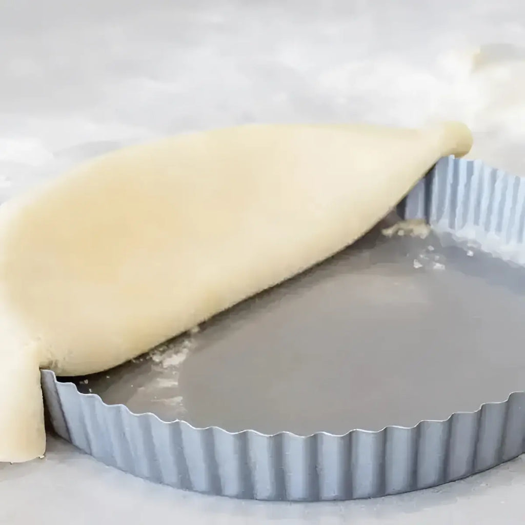 A pale pie crust shaped over a gray kitchencraft non-stick loose base flan tin 24.5cm for quiche baking