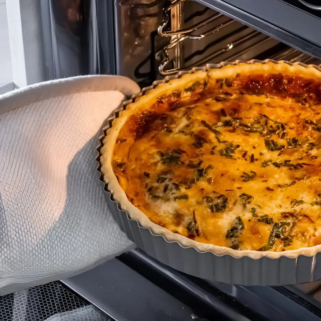 Golden-brown quiche in a dark gray KitchenCraft non-stick loose base flan quiche tin 24.5cm topped with herbs and cheese