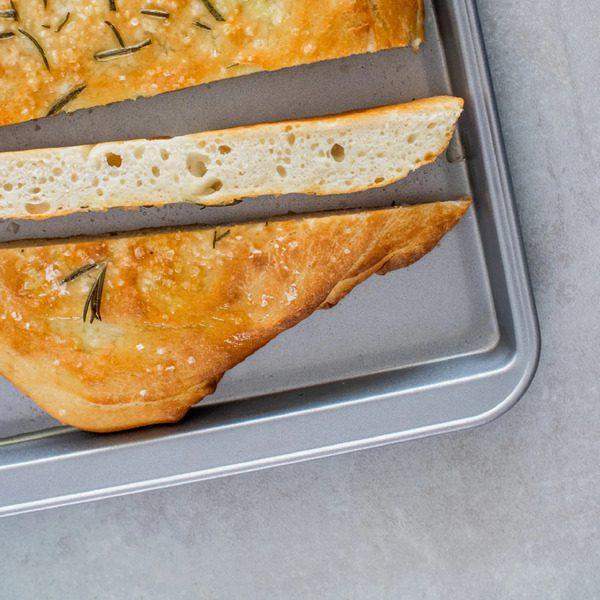 KitchenCraft non-stick oven tray 43cm holding golden-brown rosemary focaccia bread slices with soft airy interior and herbs