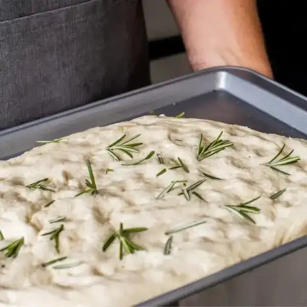 Unbaked focaccia dough with fresh rosemary in a KitchenCraft non-stick 43cm rectangular oven tray