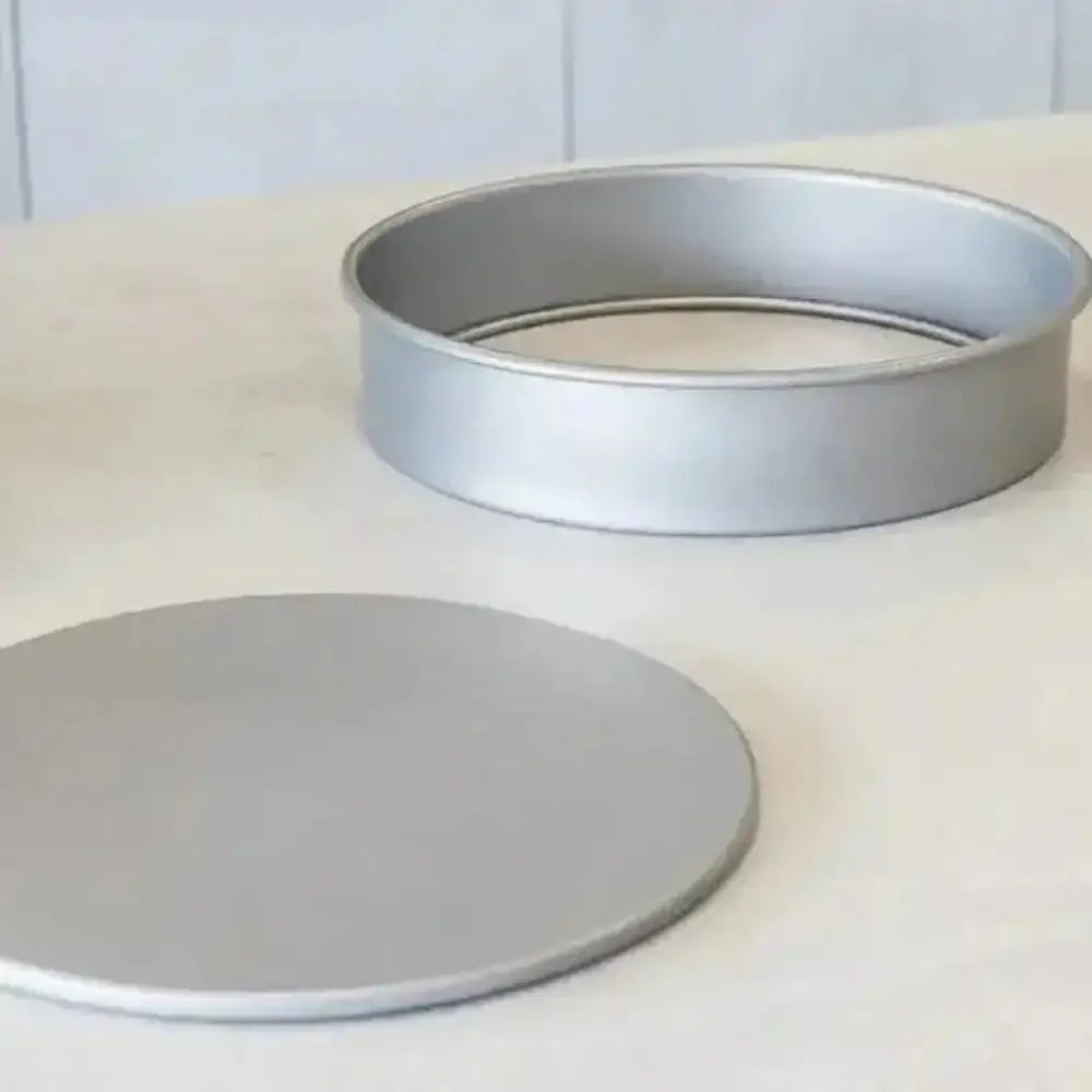 Two metal cake pans on a white surface with a light blue tiled wall background.