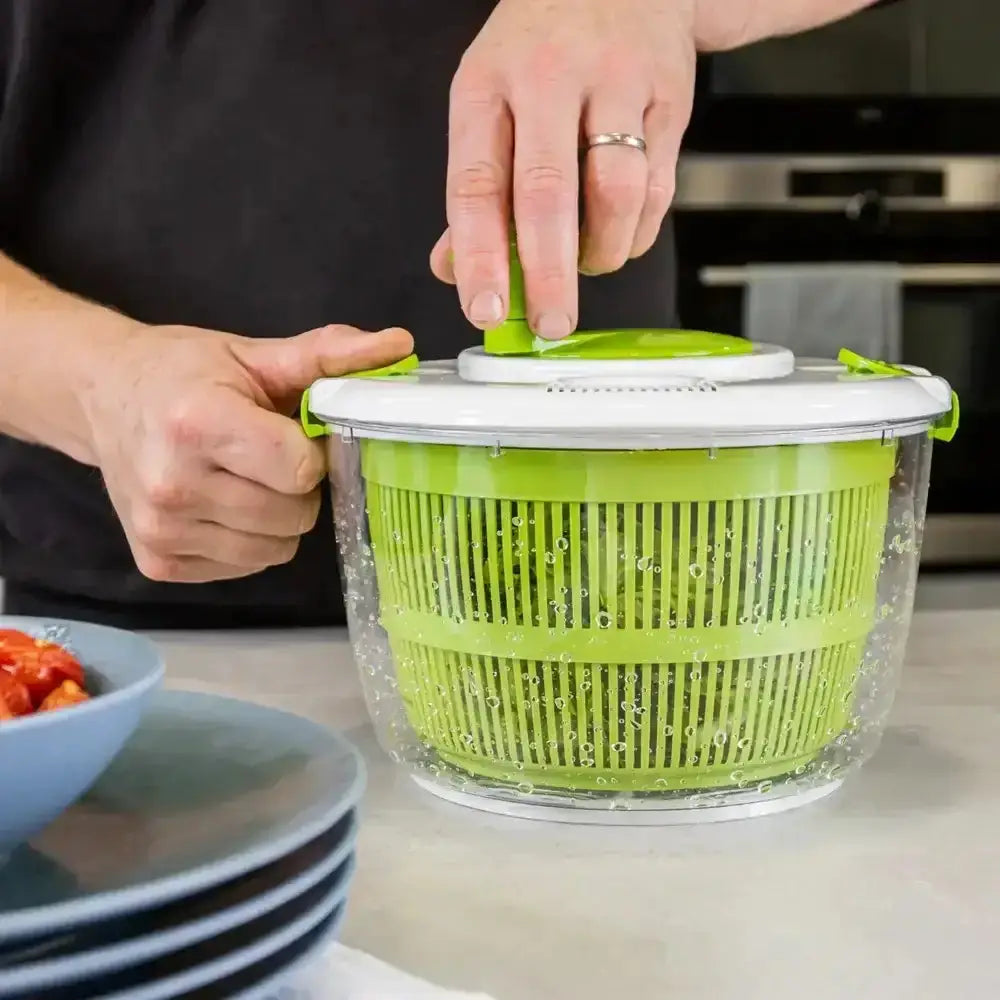 Person using a green salad spinner on a kitchen counter.
