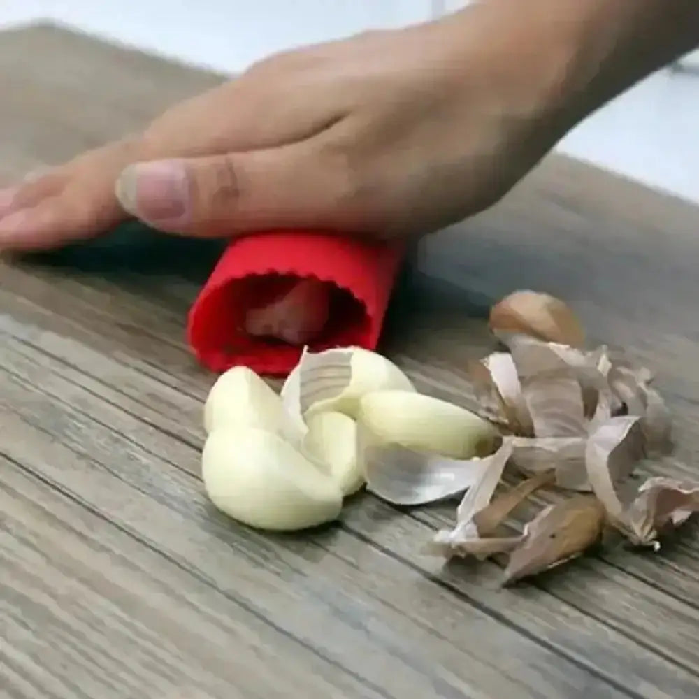 Hand using a red garlic peeler on a wooden surface with garlic cloves.
