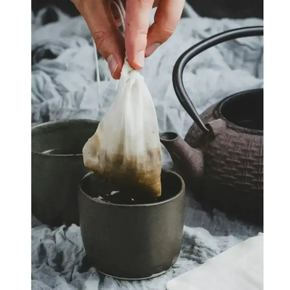 Tea bag being removed from a cup with a teapot in the background