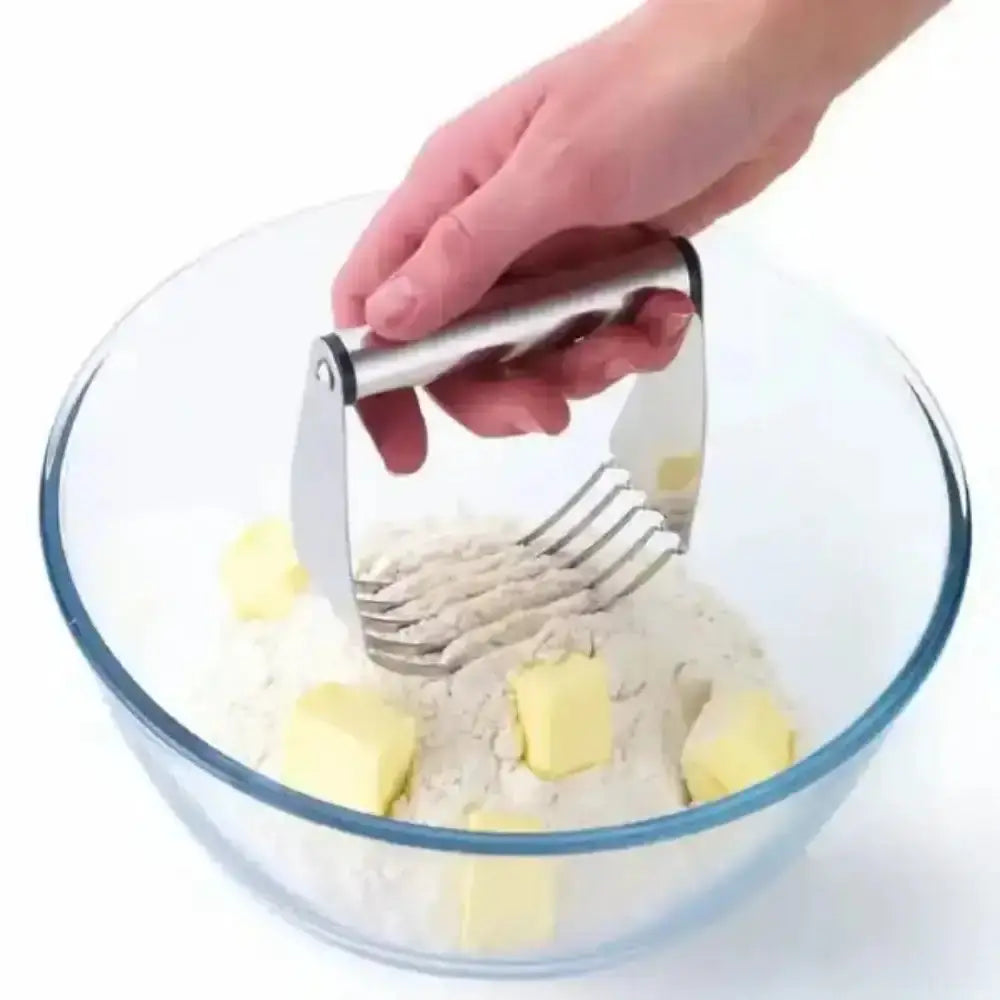 Hand using a pastry cutter to cut butter into flour in a glass bowl.