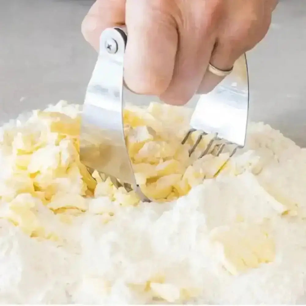 Hand using a metal tool to mash potatoes in a bowl