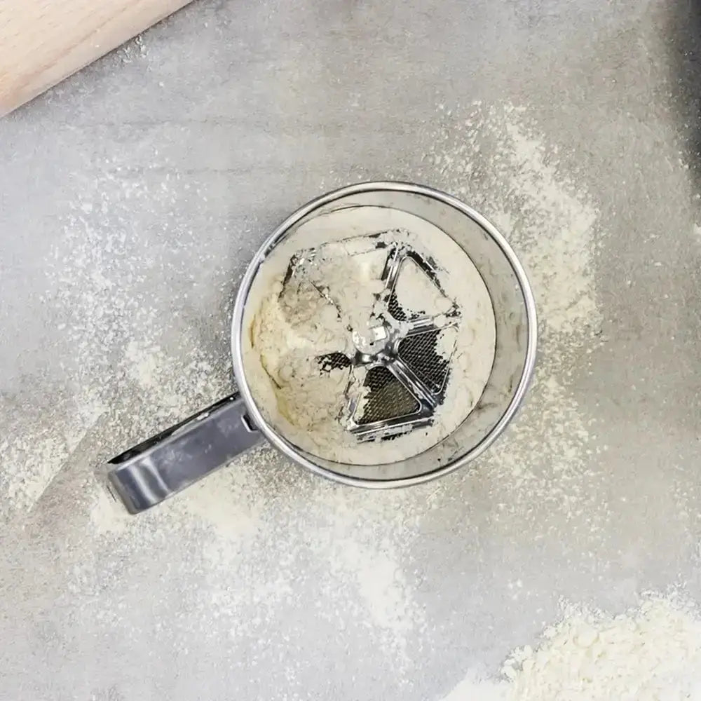 Metal sifter with flour on a gray surface