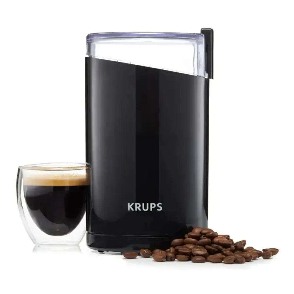 Black KRUPS coffee grinder with a glass of coffee and coffee beans on a white background
