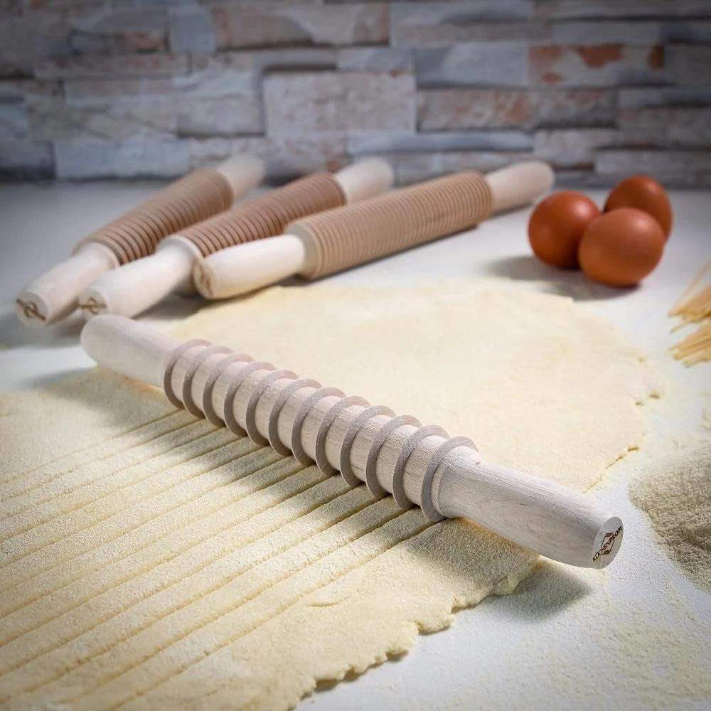 Wooden pasta rolling pins on a surface with rolled-out dough and tomatoes in the background.