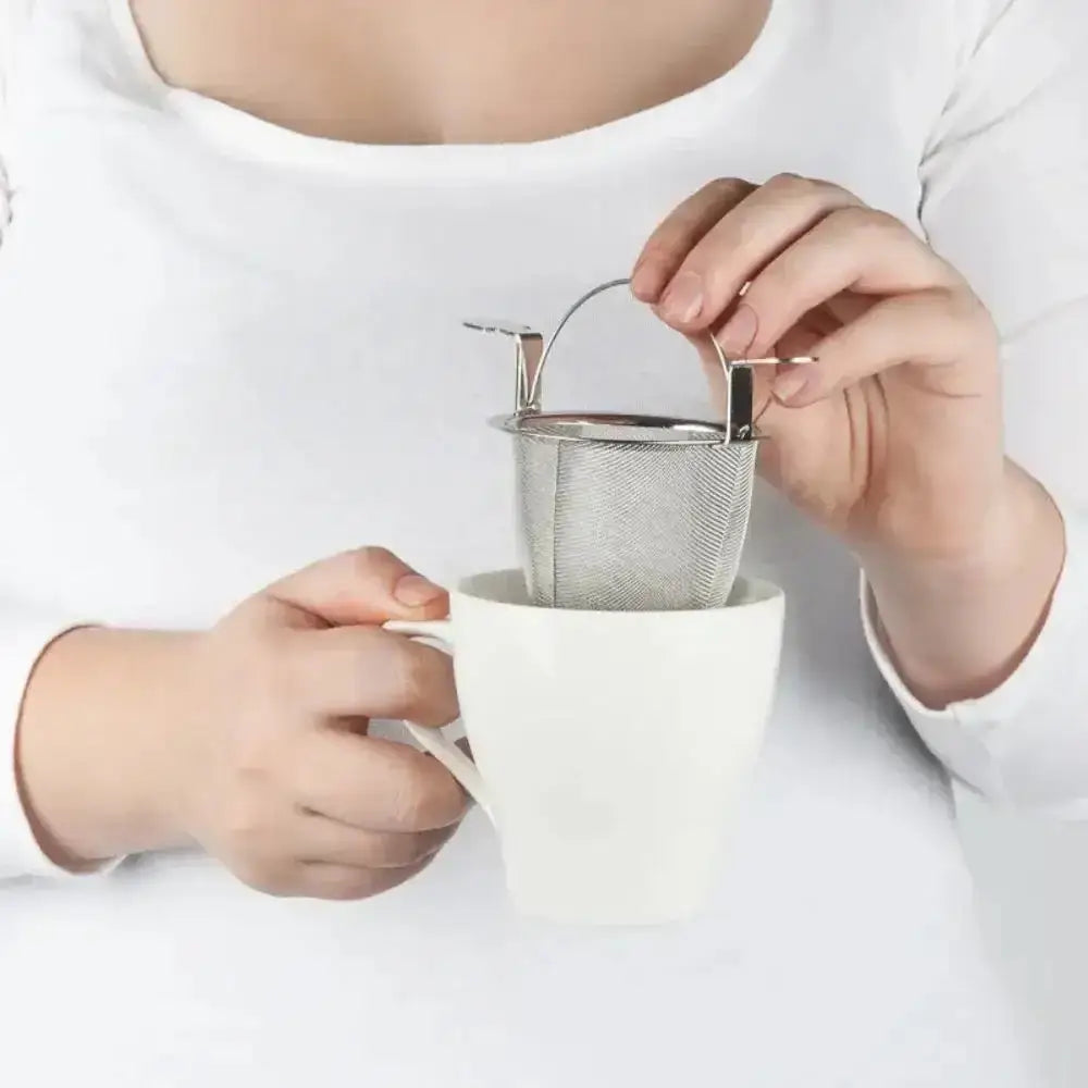 Person holding a white mug with a metal tea infuser.