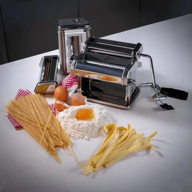 Pasta maker with fresh pasta, flour, and eggs on a white surface