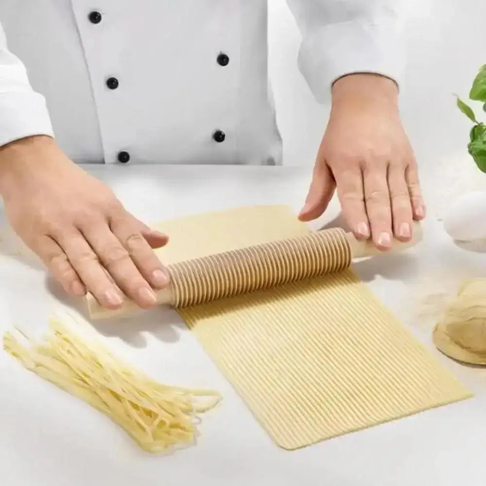 Person using a pasta roller to make pasta on a white surface.