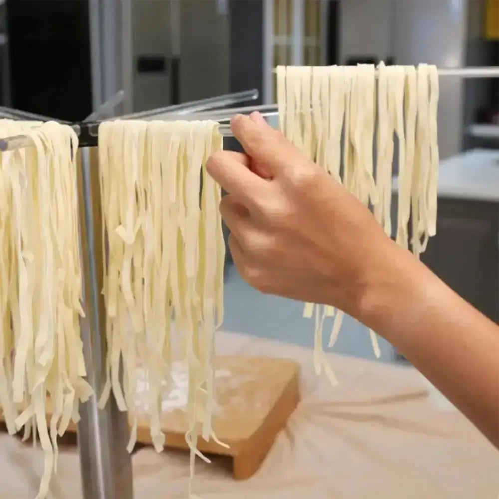 Hand adjusting fresh pasta on a drying rack in a kitchen.