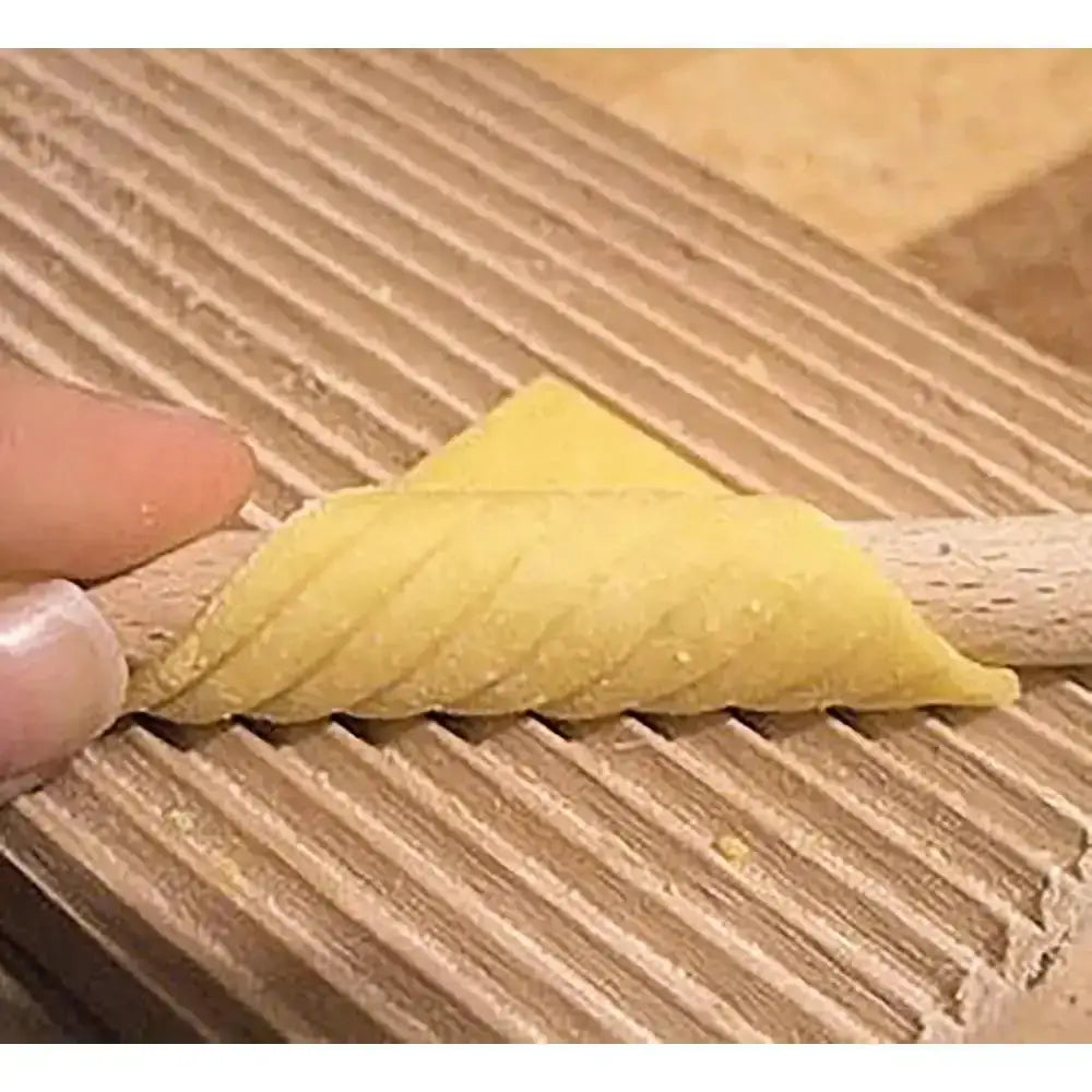 Hand holding a triangular piece of dough over a wooden surface with a textured pattern.
