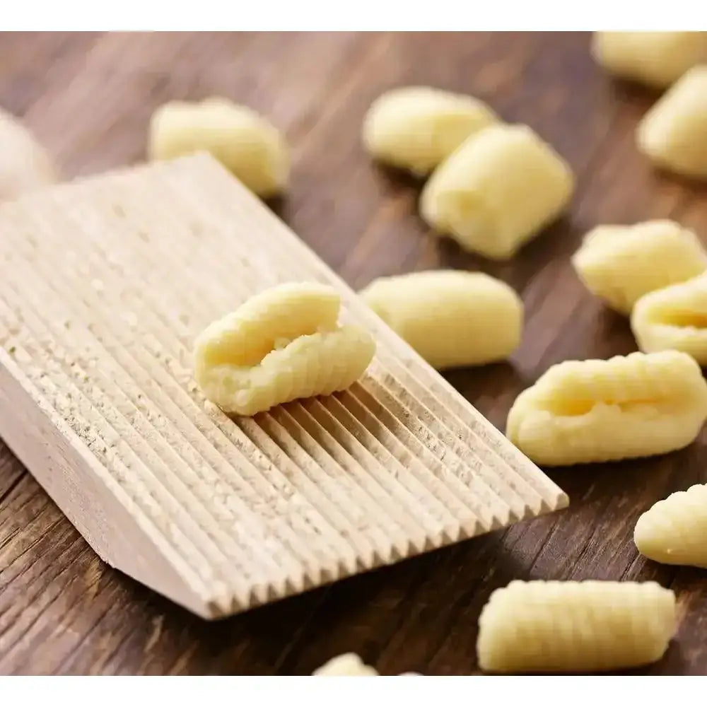 Wooden gnocchi maker with freshly made gnocchi on a wooden surface