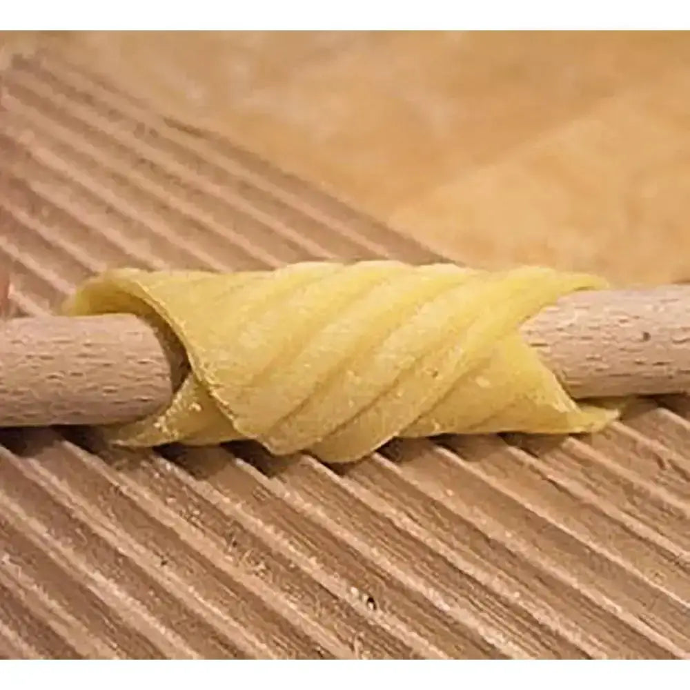 Pasta dough being rolled out with a wooden roller on a wooden surface