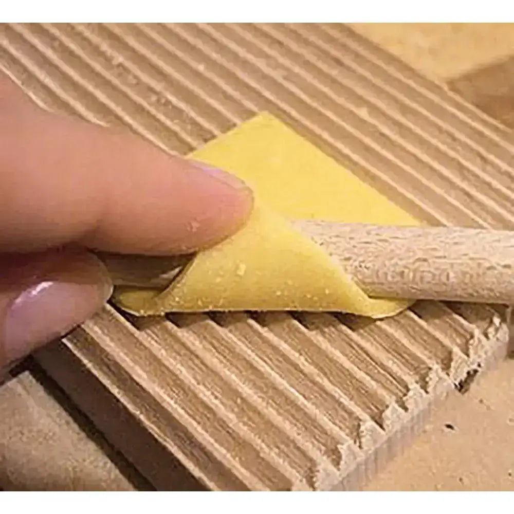Hand rolling yellow pasta dough with a wooden roller on a wooden surface